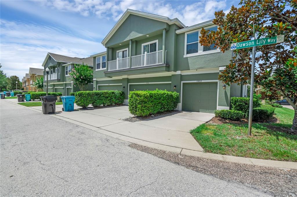 A row of green two-story townhomes with attached garages and manicured hedges along the street — 10802 ECLIPSE LILY WAY UNIT 50A, ORLANDO, FL