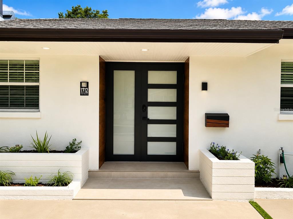 A modern home exterior features a white facade, a dark double door, and two planters — 1712 INDIAN ROCKS ROAD, BELLEAIR, FL