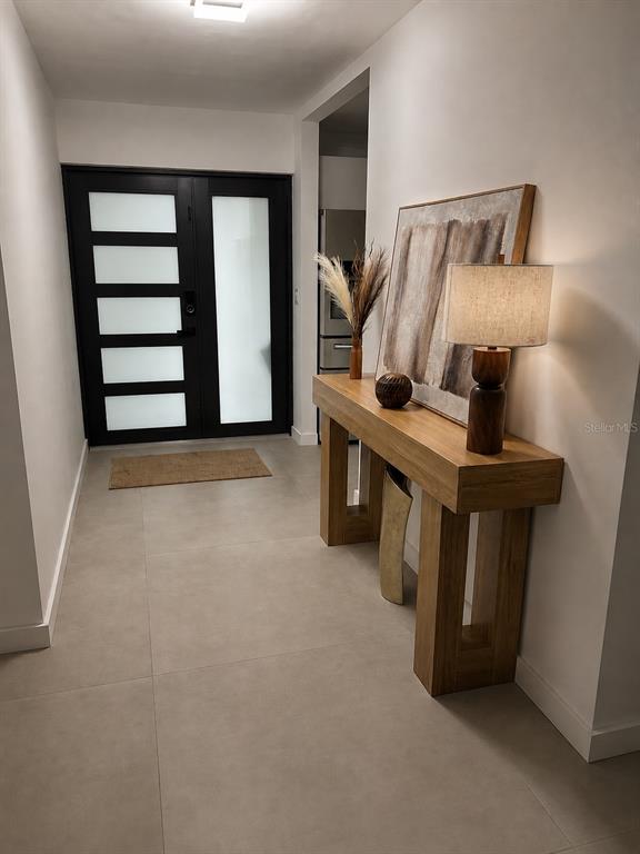 A modern entryway features large-format tile flooring, a dark-framed glass door, and a wooden console table — 1712 INDIAN ROCKS ROAD, BELLEAIR, FL