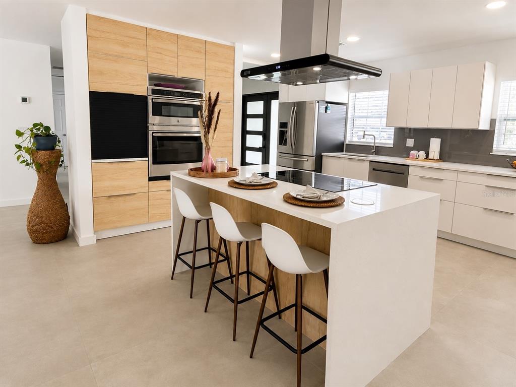 A modern kitchen features a white island with bar stools, light wood cabinetry, and stainless appliances — 1712 INDIAN ROCKS ROAD, BELLEAIR, FL