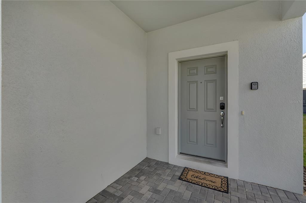 A gray front door with a welcome mat sits on a paved porch entryway — 2201 LELANI CIRCLE, DAVENPORT, FL