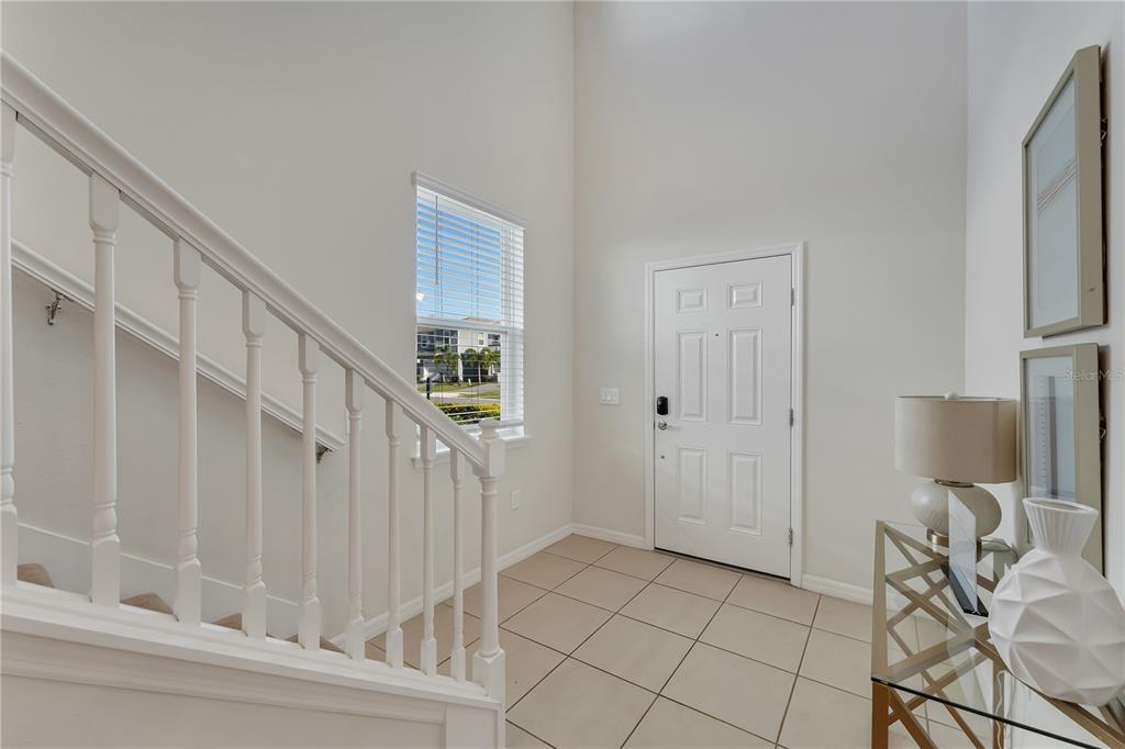 A bright entryway features white walls, tile flooring, a staircase with white railings, and a door — 2201 LELANI CIRCLE, DAVENPORT, FL