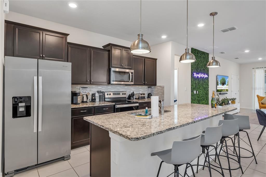 A kitchen features dark wood cabinets, granite countertops, a stainless steel refrigerator, and a breakfast island — 2201 LELANI CIRCLE, DAVENPORT, FL