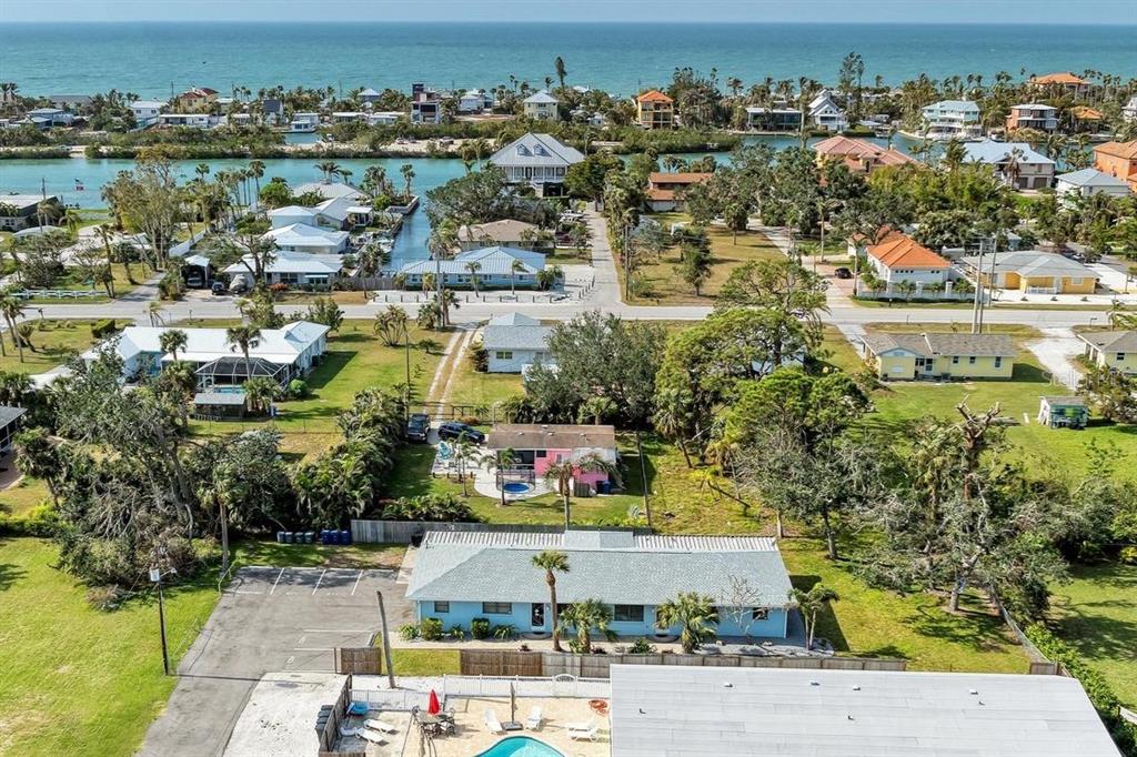 An aerial view shows a coastal neighborhood with houses, a canal, and the ocean beyond — 401 SHORE ROAD, NOKOMIS, FL