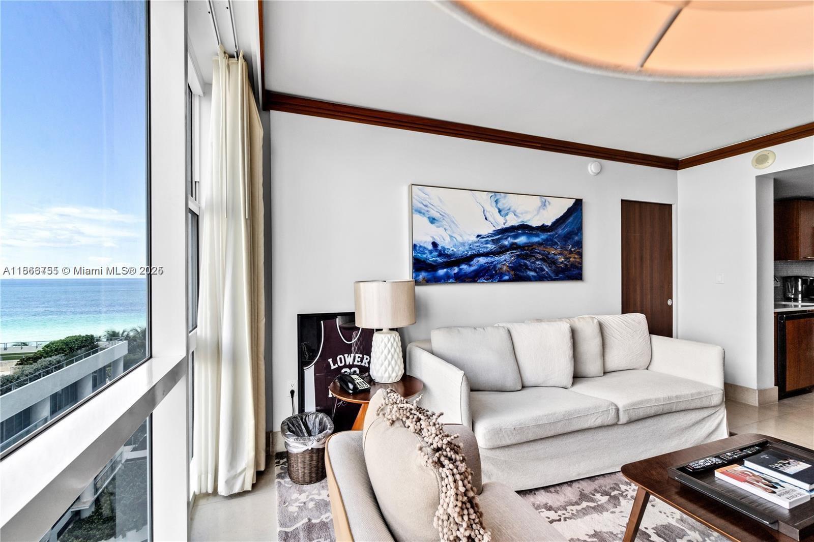 A living room features a white sofa, ocean views, and a framed jersey near a window — 6801 Collins Ave # 818, Miami Beach FL 33141, MIAMI BEACH, FL