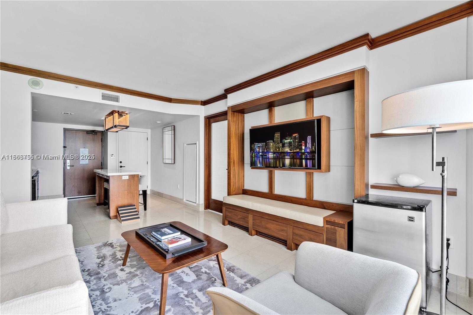 A living room features a wall-mounted television, wooden built-in cabinetry, and a small kitchenette area — 6801 Collins Ave # 818, Miami Beach FL 33141, MIAMI BEACH, FL