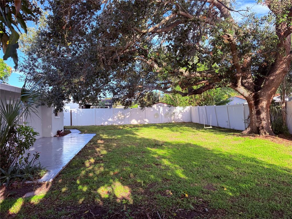 A grassy backyard features a large oak tree with a swing and a white fence — 5919 33RD AVENUE N, ST PETERSBURG, FL