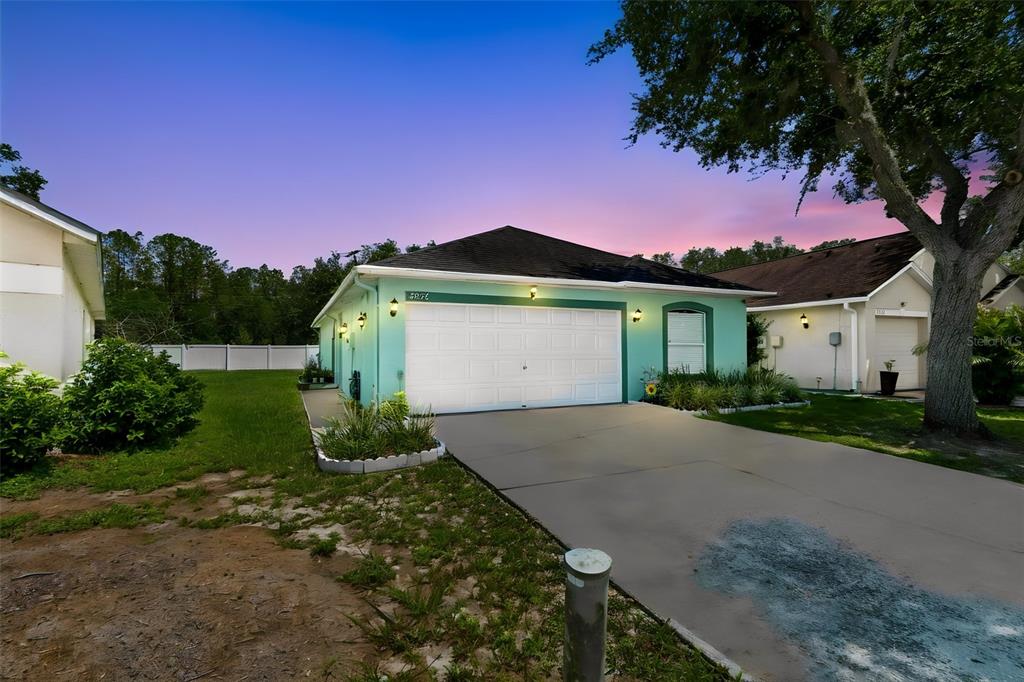 A teal-colored house with a white garage door and a concrete driveway at dusk — 5936 LAKE FRONT DRIVE, WESLEY CHAPEL, FL