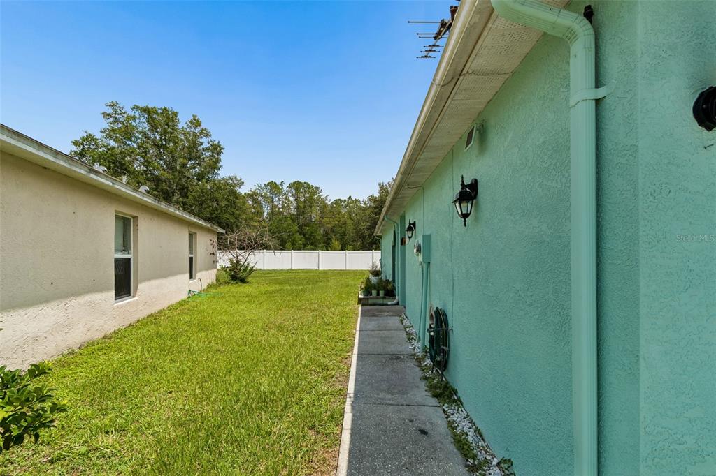 A side yard with a concrete walkway between two houses and a white privacy fence — 5936 LAKE FRONT DRIVE, WESLEY CHAPEL, FL