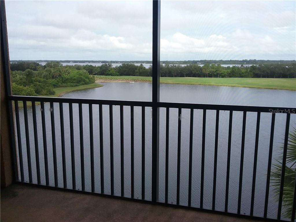 A screened balcony overlooks a lake and a grassy landscape under a cloudy sky — 6515 GRAND ESTUARY TRAIL UNIT 402, BRADENTON, FL