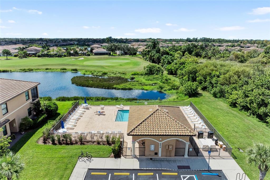 An aerial view shows a community pool area with a clubhouse, lounge chairs, and a pond — 6515 GRAND ESTUARY TRAIL UNIT 402, BRADENTON, FL