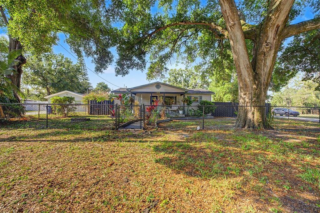 A single-story house with a fenced yard and large oak trees under a blue sky — 1318 W RAMBLA STREET, TAMPA, FL