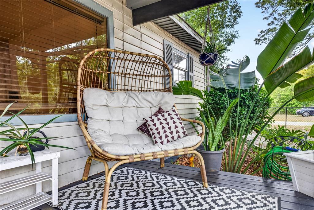 A rattan loveseat sits on a wooden porch with a patterned rug and potted plants — 1318 W RAMBLA STREET, TAMPA, FL
