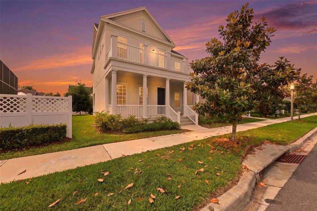 A two-story house with a front porch and balcony stands beside a sidewalk at sunset — 7410 BARRIER COVE WAY, KISSIMMEE, FL