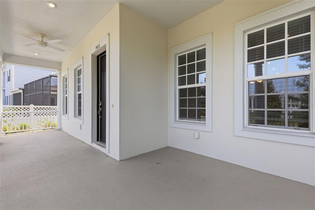 A covered porch features a dark front door, white trim, and a ceiling fan — 7410 BARRIER COVE WAY, KISSIMMEE, FL