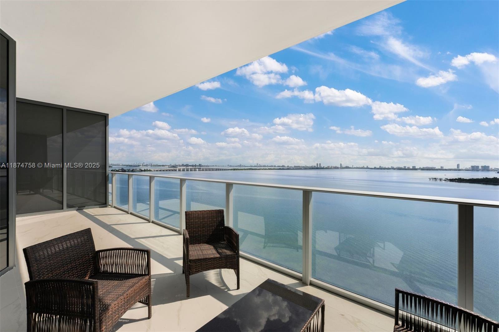 A balcony with wicker furniture overlooks a large body of water under a blue sky — 700 NE 24th St # 1005, Miami FL 33137, MIAMI, FL