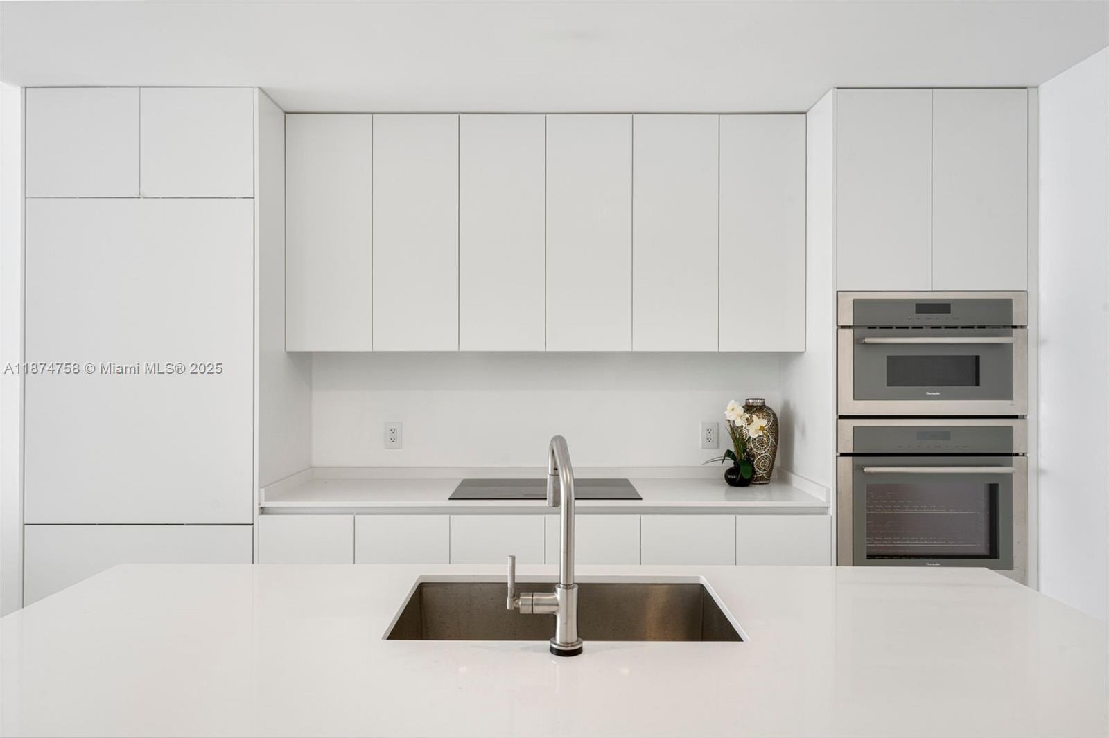 A modern kitchen features white cabinetry, a stainless steel sink, and built-in wall ovens — 700 NE 24th St # 1005, Miami FL 33137, MIAMI, FL