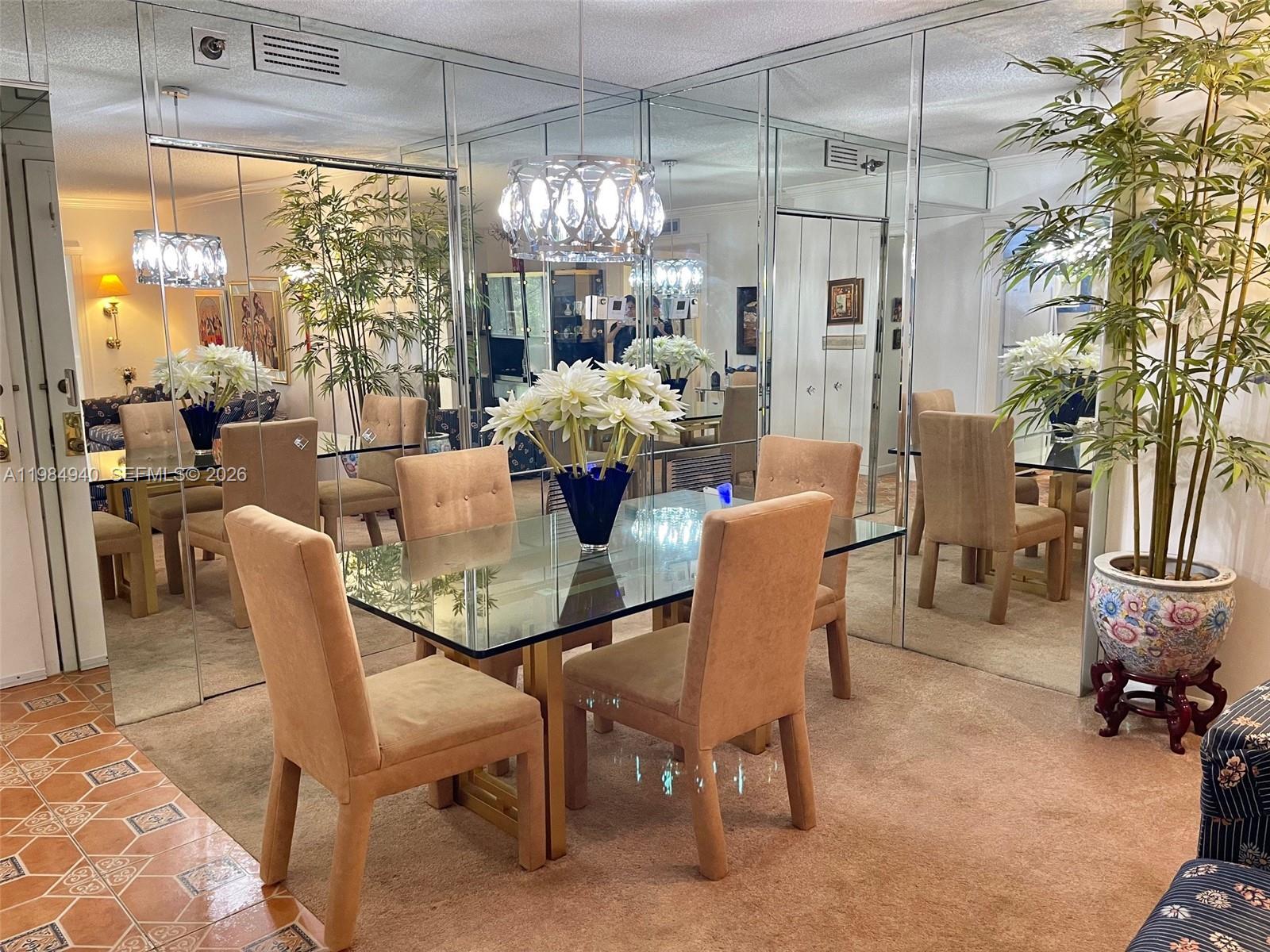 A dining room features a glass-topped table, upholstered chairs, mirrored walls, and a potted plant — 3850 Washington St # 214, Hollywood FL 33021, HOLLYWOOD, FL