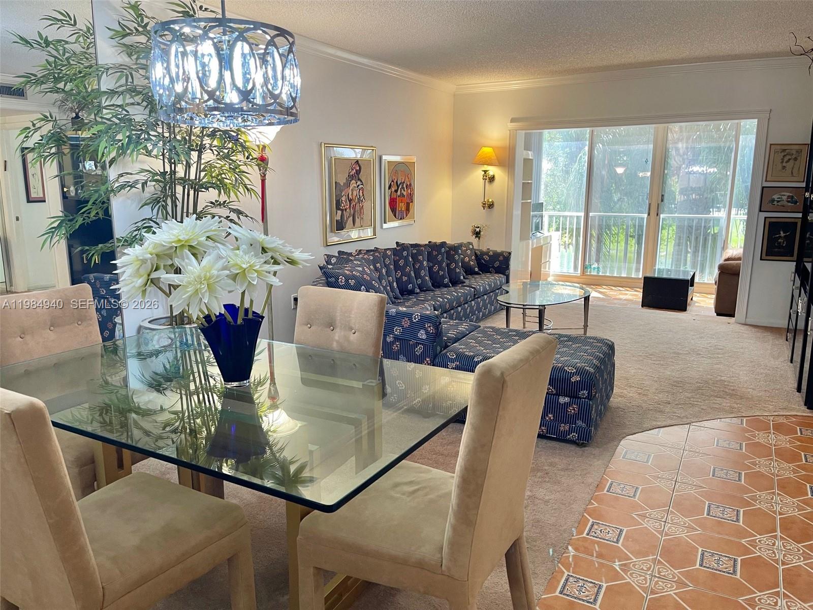 A dining area with a glass table overlooks a living room featuring patterned blue furniture — 3850 Washington St # 214, Hollywood FL 33021, HOLLYWOOD, FL