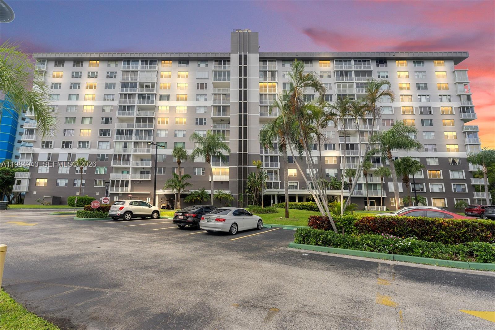 A multi-story apartment building with a parking lot and palm trees at sunset — 3850 Washington St # 214, Hollywood FL 33021, HOLLYWOOD, FL