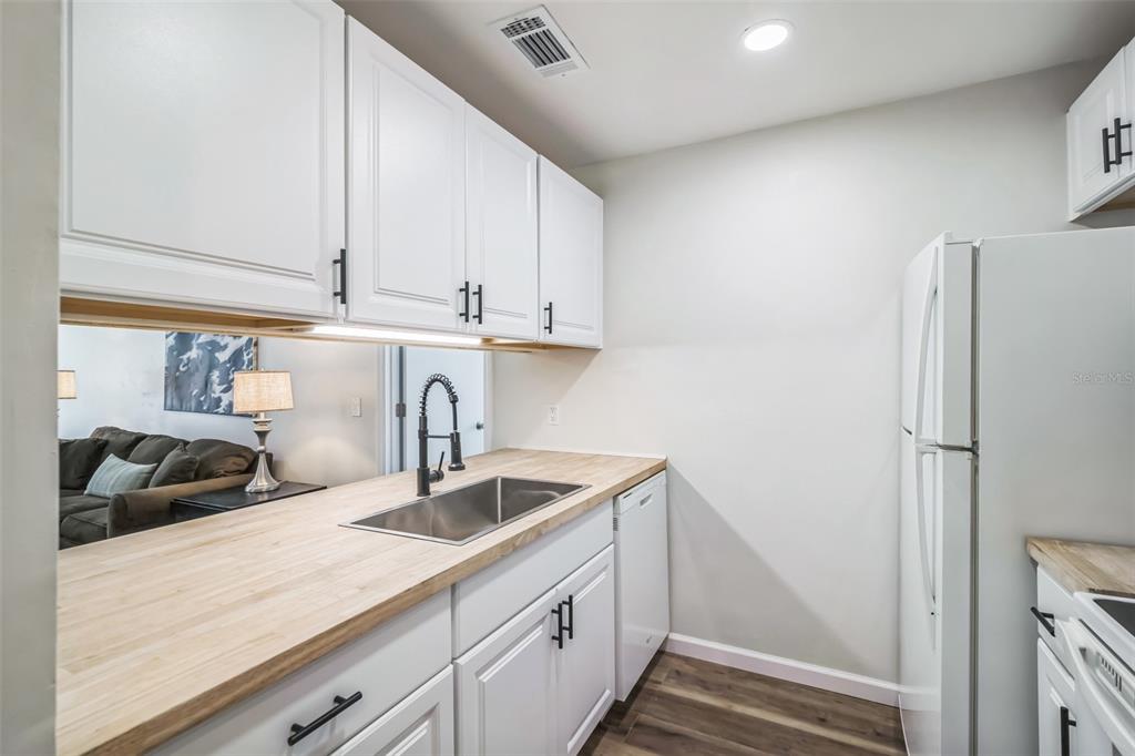 A kitchen features white cabinets, a butcher block countertop, a stainless steel sink, and appliances — 3800 SW 20TH AVENUE UNIT 112, GAINESVILLE, FL