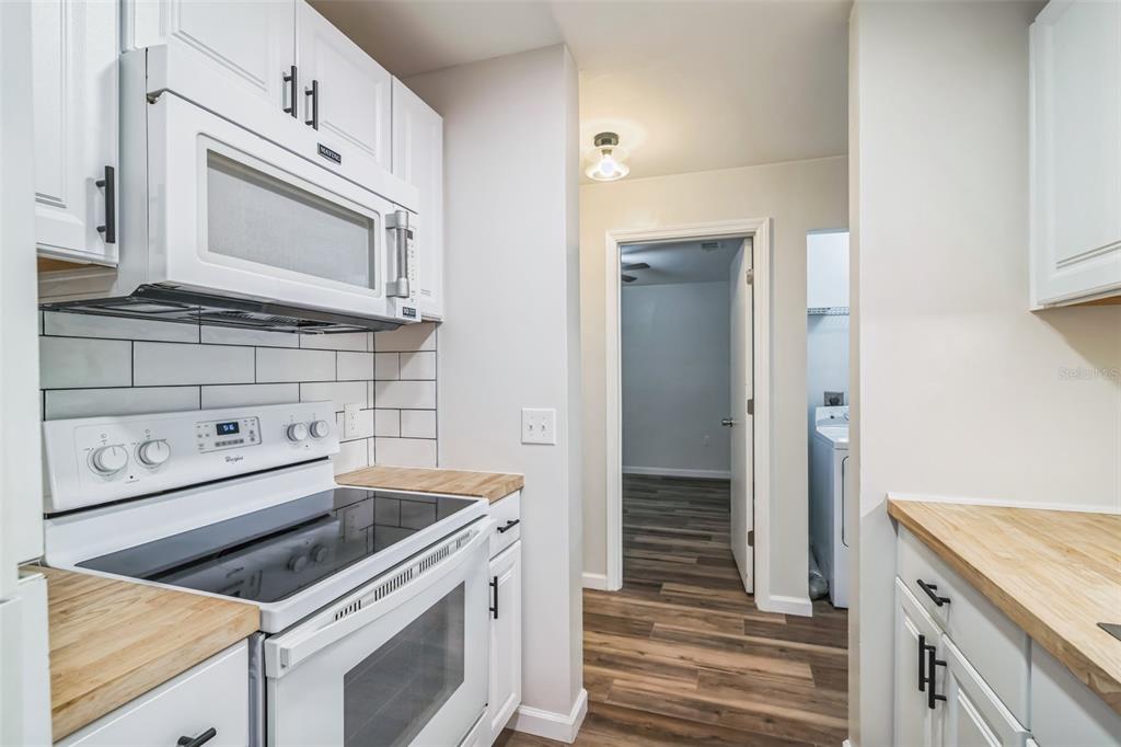 A kitchen features white cabinets, a white stove, a microwave, and light wood countertops — 3800 SW 20TH AVENUE UNIT 112, GAINESVILLE, FL