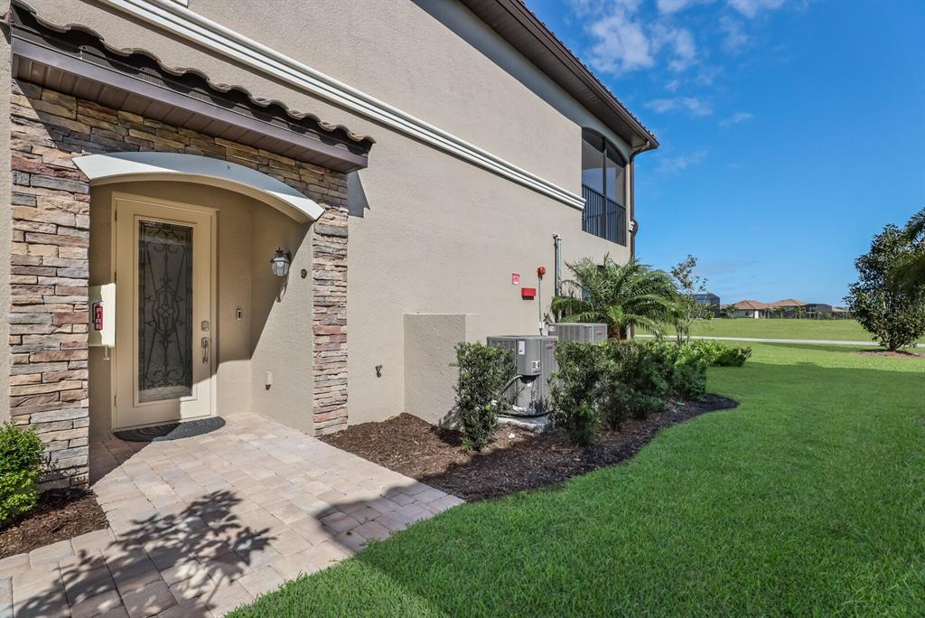 The exterior of a tan stucco building features a stone-accented entryway and two HVAC units — 18017 GAWTHROP DRIVE UNIT 104, BRADENTON, FL