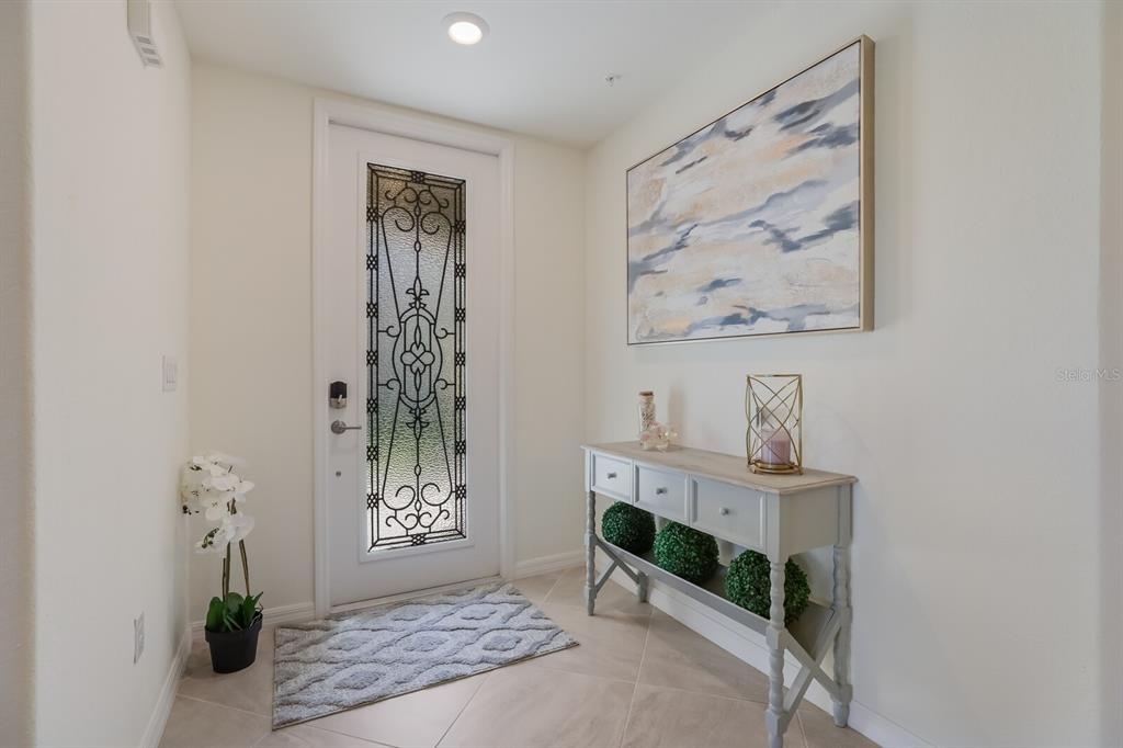 An entryway features a white door with decorative glass, a console table, and abstract art — 18017 GAWTHROP DRIVE UNIT 104, BRADENTON, FL