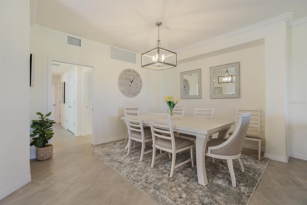 A dining room features a white table, six chairs, a chandelier, and a gray rug — 18017 GAWTHROP DRIVE UNIT 104, BRADENTON, FL