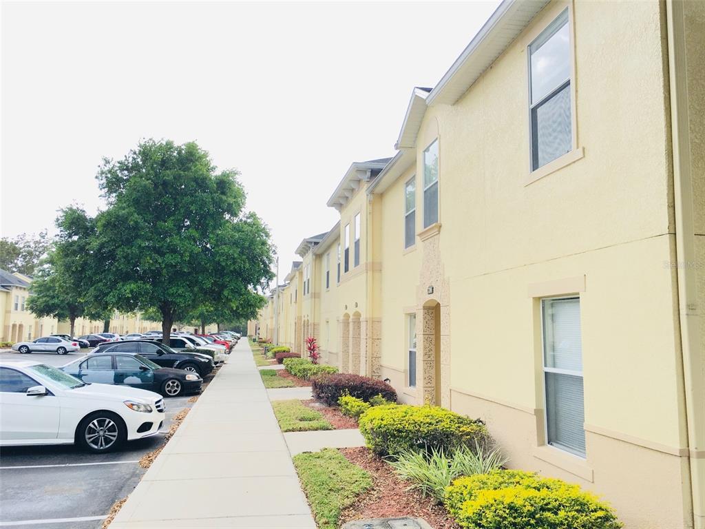 A sidewalk runs alongside a row of yellow townhomes with parked cars in the foreground — 2764 CLUB CORTILE CIRCLE, KISSIMMEE, FL