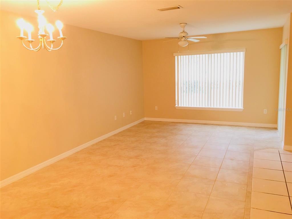 An empty room features beige walls, light-colored tile flooring, a ceiling fan, and a chandelier — 2764 CLUB CORTILE CIRCLE, KISSIMMEE, FL