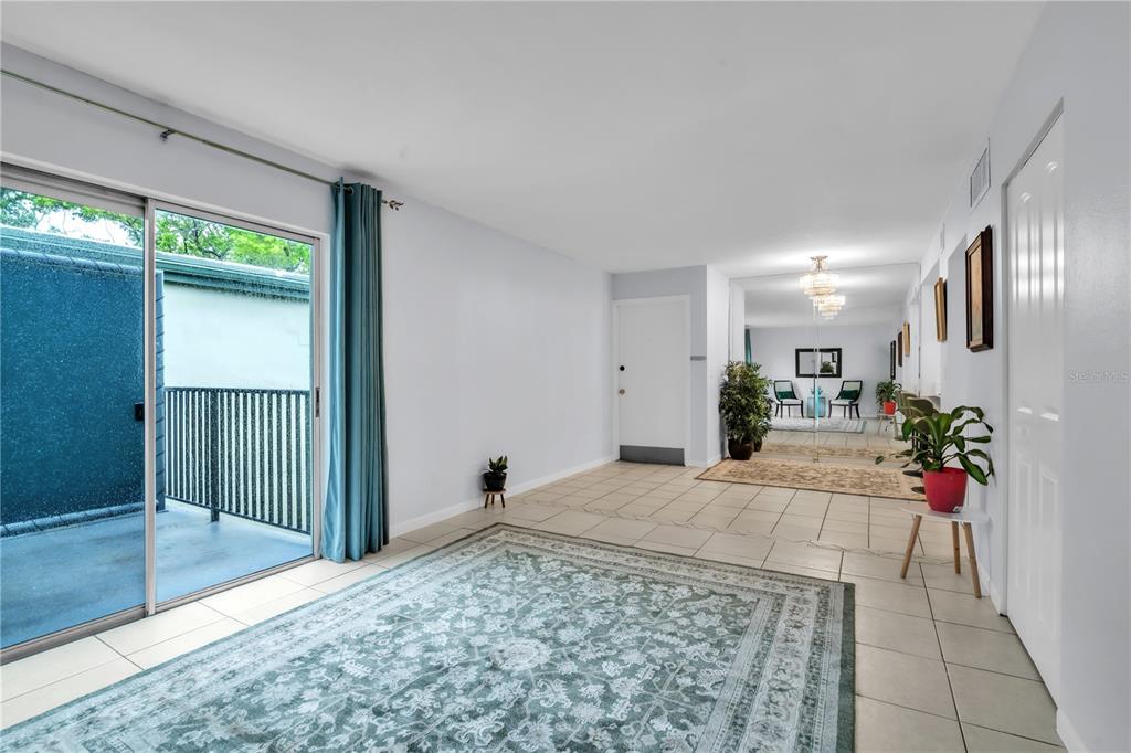 A living room with tile floors, a large area rug, sliding glass doors, and mirrored walls — 1799 N HIGHLAND AVENUE UNIT 22, CLEARWATER, FL