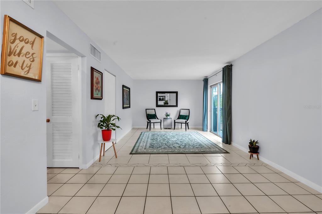 A living room with light-colored tile flooring, a large area rug, and sliding glass doors — 1799 N HIGHLAND AVENUE UNIT 22, CLEARWATER, FL