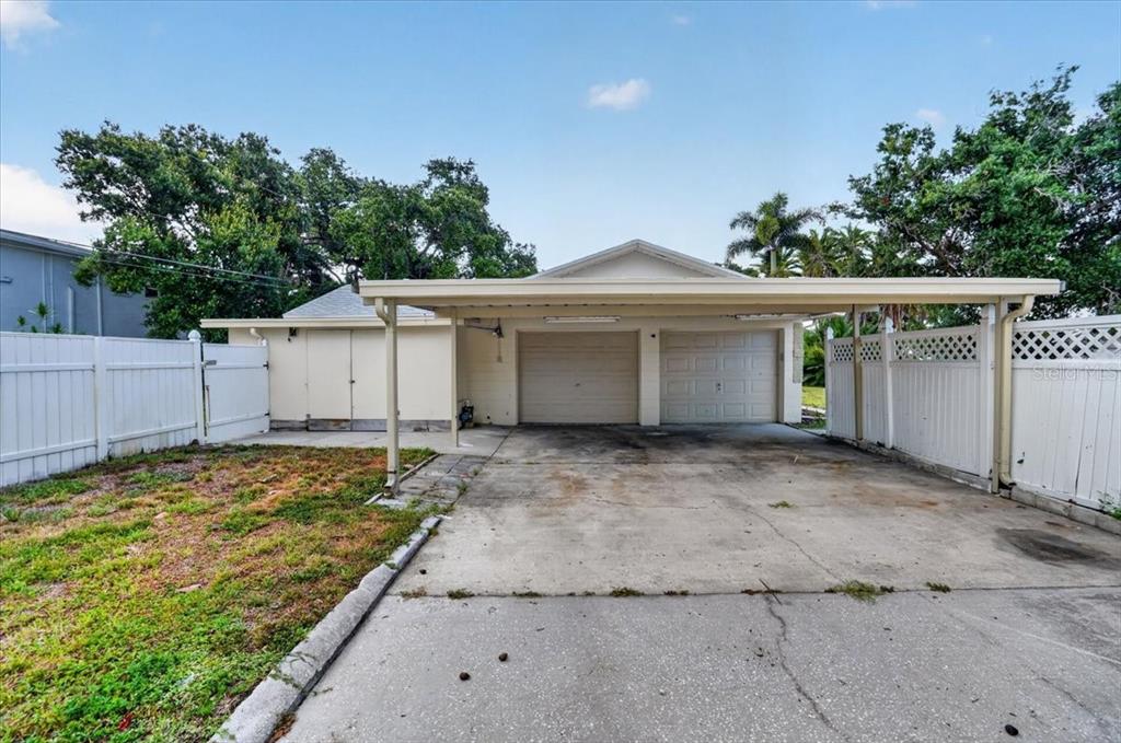 A detached garage with a carport sits on a concrete driveway behind a white fence — 6999 16TH AVENUE N, ST PETERSBURG, FL