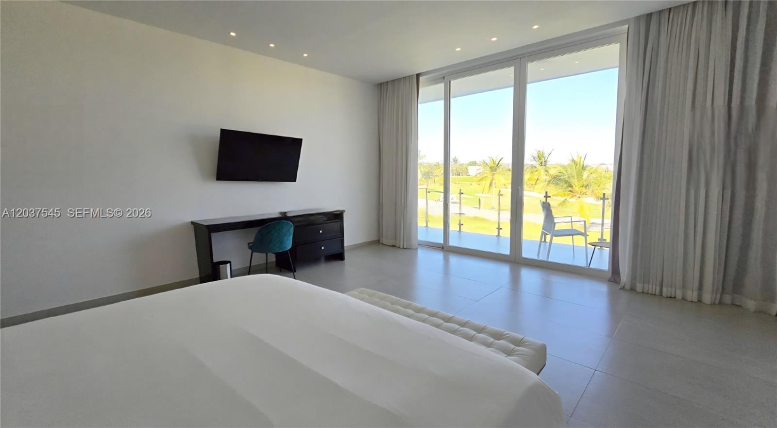 A bedroom features a white bed, a desk with a chair, and a balcony view — 0 la palmass, FL