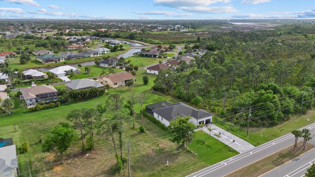 An aerial view shows a suburban house with a screened pool near a wooded area — 170 ROTONDA BOULEVARD E, ROTONDA WEST, FL