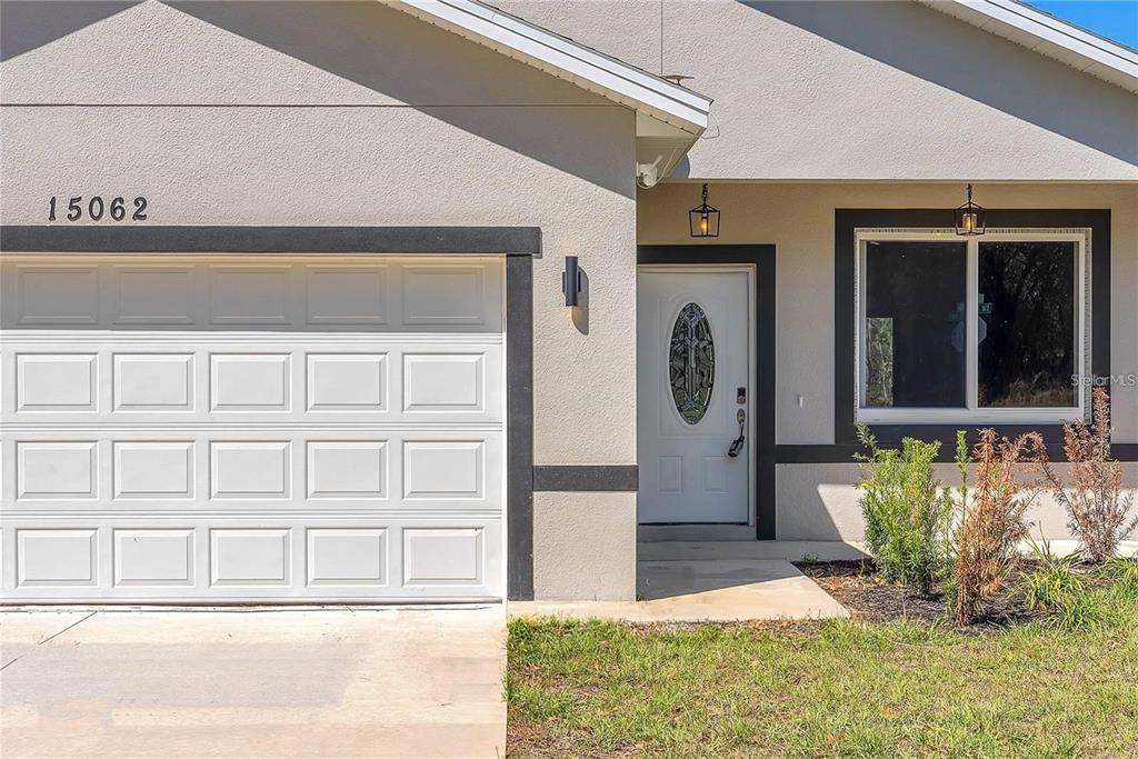The exterior of a house features a white garage door, a front door, and a window — 15062 SW 63RD COURT ROAD, OCALA, FL