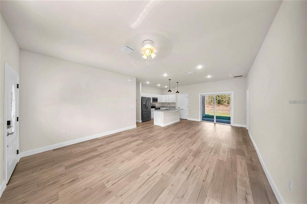 An open-concept living area features light wood-look flooring, neutral walls, and a kitchen with white cabinetry — 15062 SW 63RD COURT ROAD, OCALA, FL