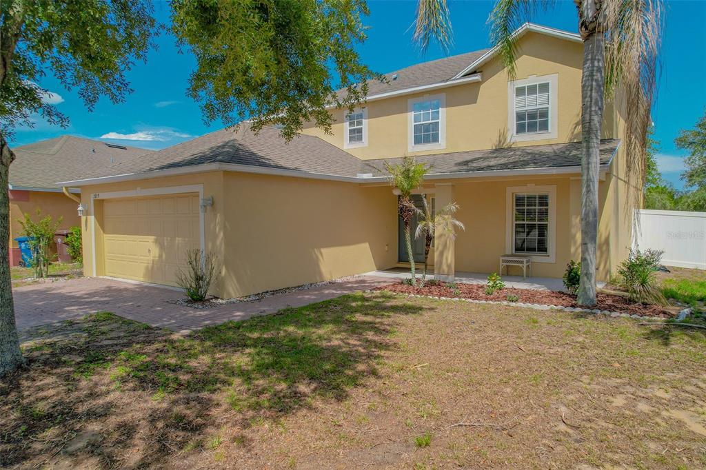 A two-story tan house with a two-car garage and a front yard with trees — 2019 HONEYBELL AVENUE, HAINES CITY, FL