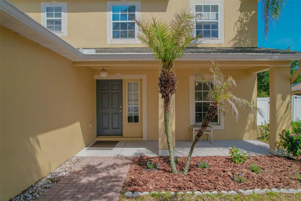 A tan two-story house exterior features a covered entryway with a gray door and palm tree — 2019 HONEYBELL AVENUE, HAINES CITY, FL