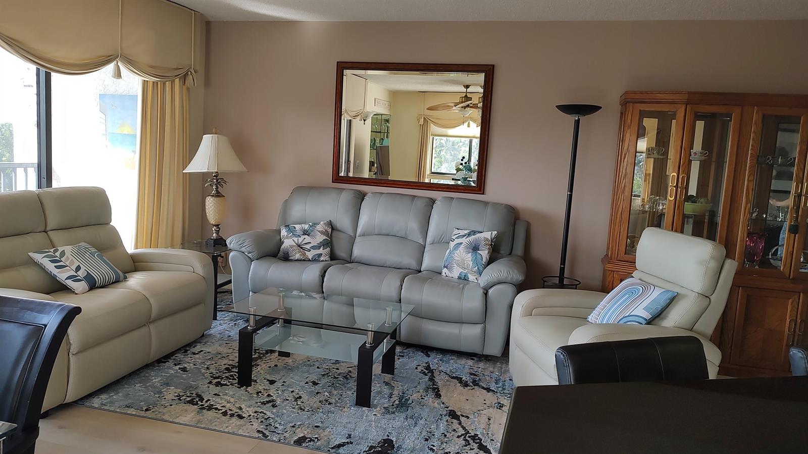 A living room features light-colored leather sofas, a glass coffee table, and a wooden hutch — 1605 S Us Highway 1 # F401, Jupiter FL 33477, JUPITER, FL