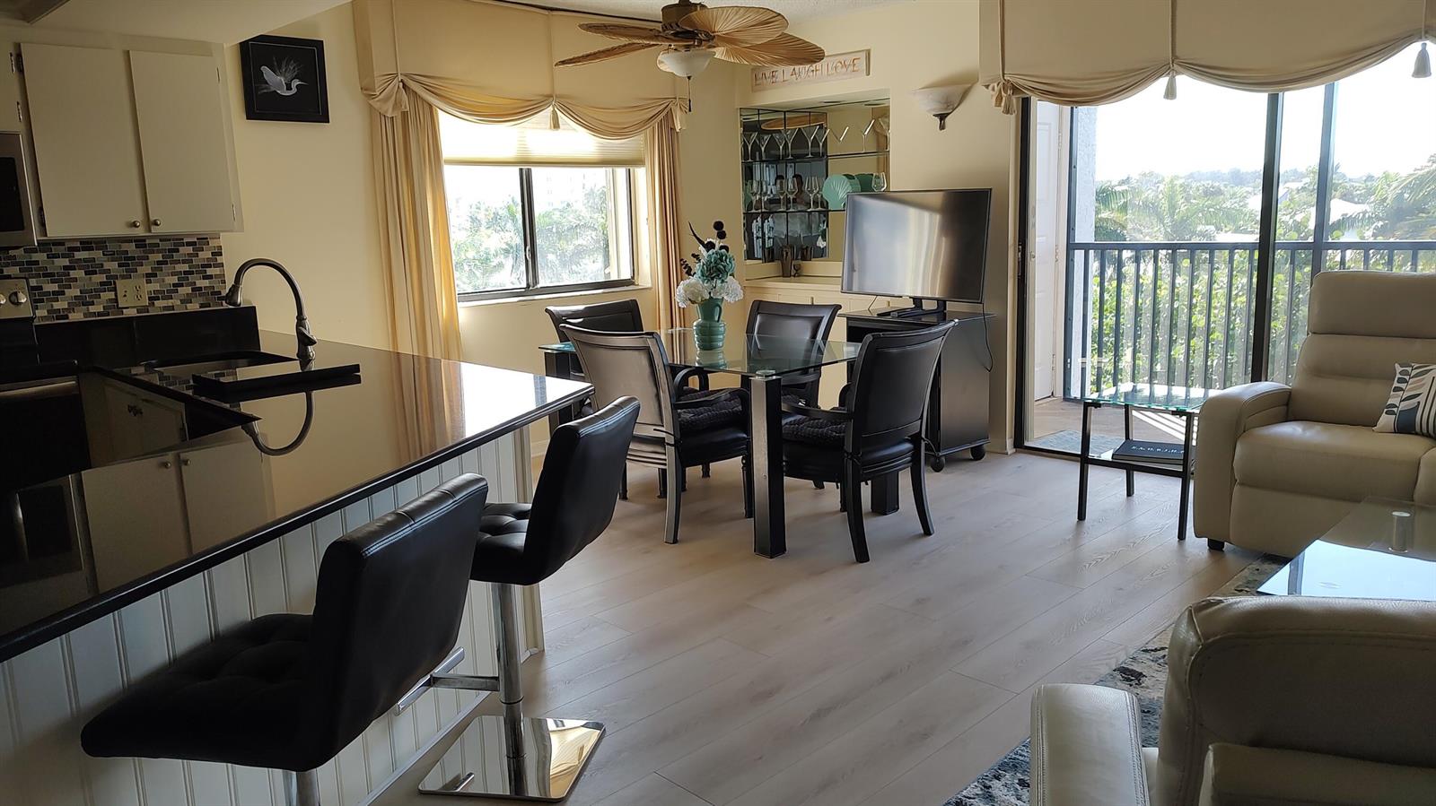 An open-concept living and dining area features a kitchen island, glass table, and balcony access — 1605 S Us Highway 1 # F401, Jupiter FL 33477, JUPITER, FL