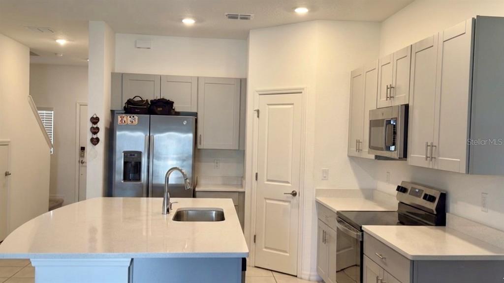 A kitchen features light gray cabinets, stainless steel appliances, and a white quartz island countertop — 2994 CANARY AVENUE, DAVENPORT, FL