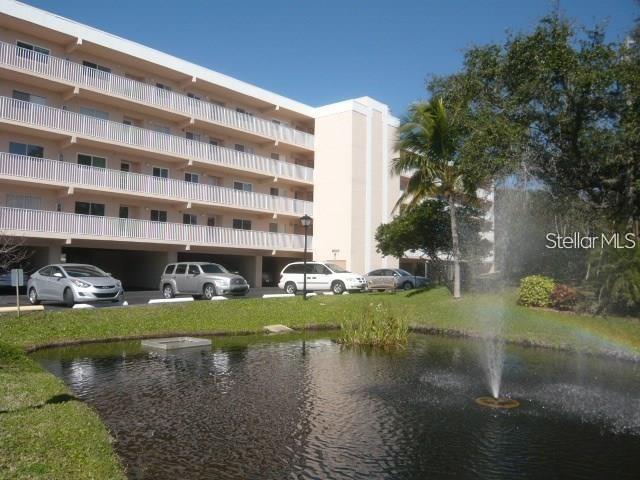 A multi-story apartment building stands behind a pond with a fountain and parked cars — 9510 HARBOR GREENS WAY UNIT 501, SEMINOLE, FL