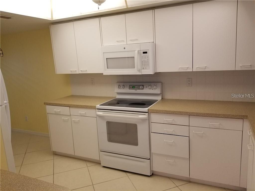 A kitchen features white cabinets, white appliances, and tan countertops over a tiled floor — 9510 HARBOR GREENS WAY UNIT 501, SEMINOLE, FL
