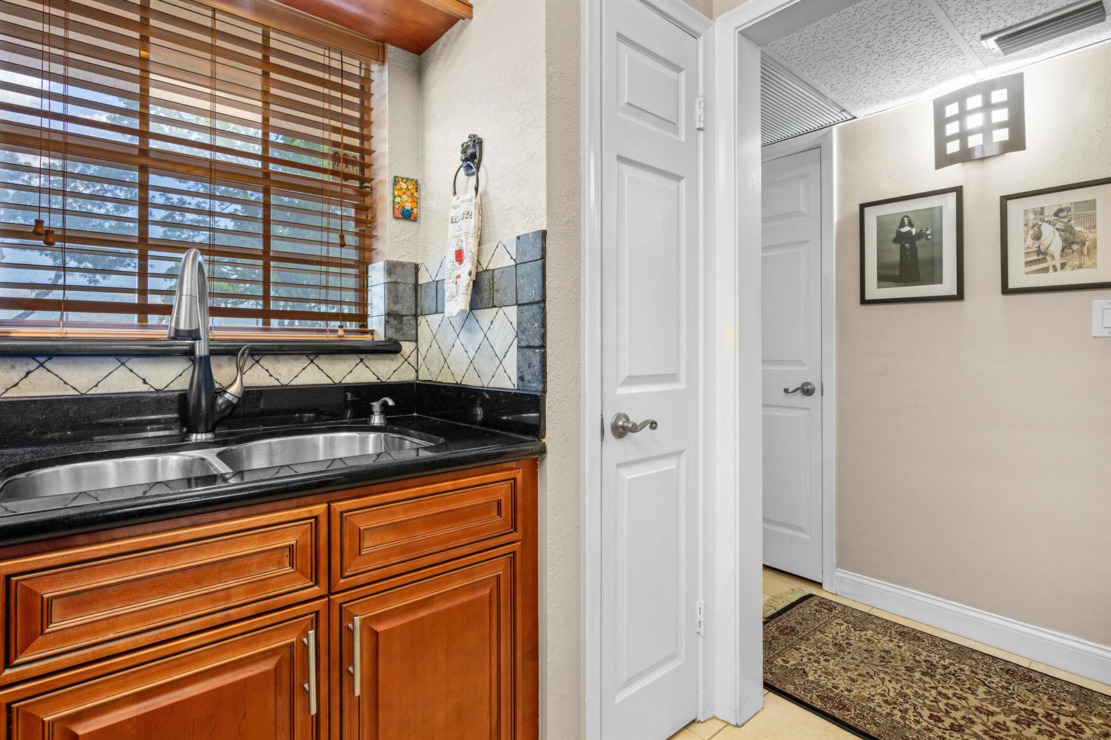 A kitchen sink with dark countertops and wood cabinets sits next to a hallway entrance — 400 NE 20th Street # B204, Boca Raton FL 33431, BOCA RATON, FL