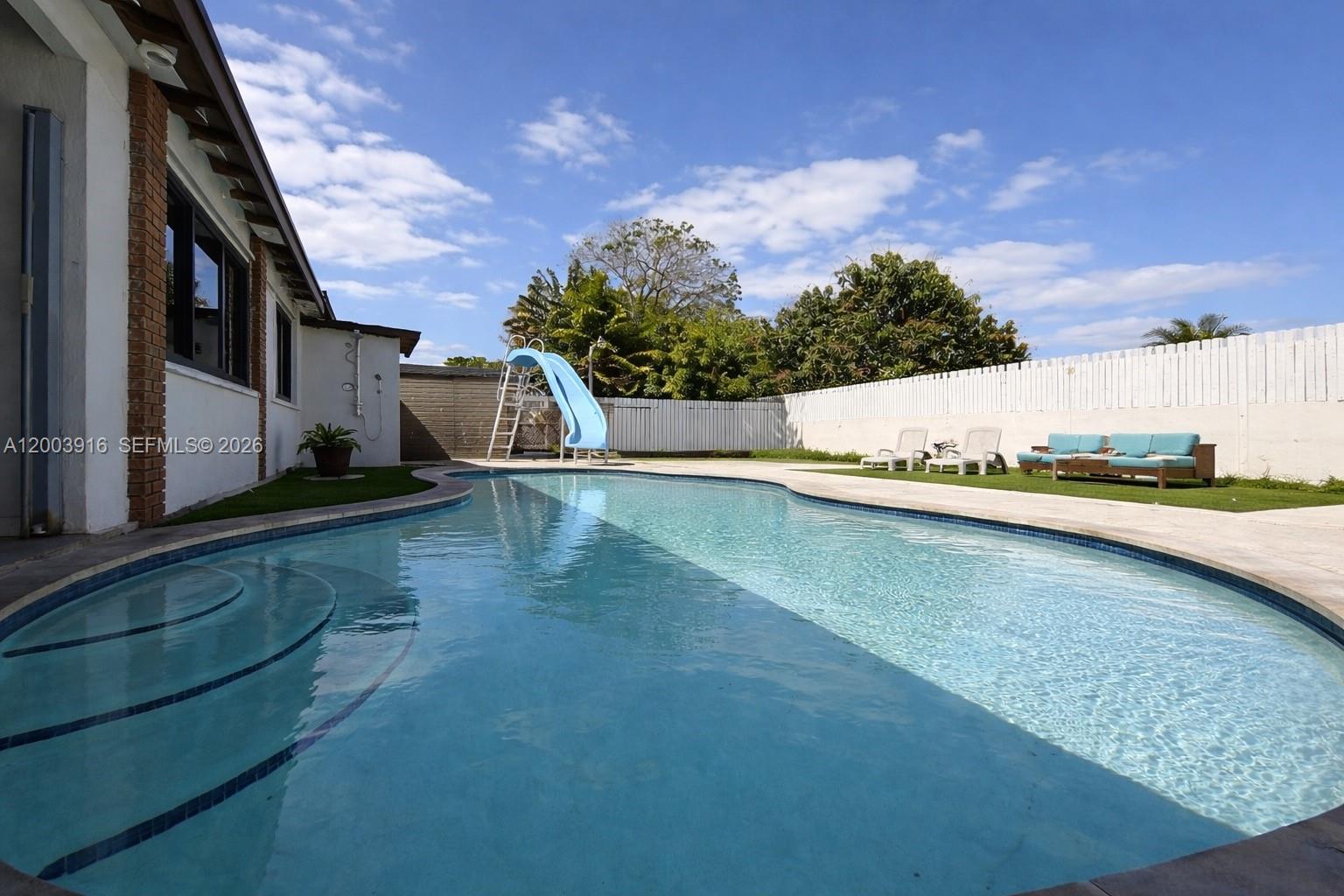 A swimming pool with a blue slide sits in a backyard next to a house — 5521 SW 132nd Ave, Miami FL 33175, MIAMI, FL