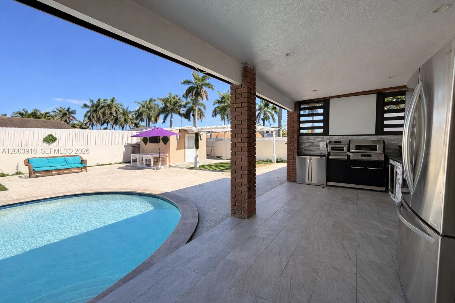 A covered outdoor kitchen overlooks a swimming pool and a patio with palm trees — 5521 SW 132nd Ave, Miami FL 33175, MIAMI, FL