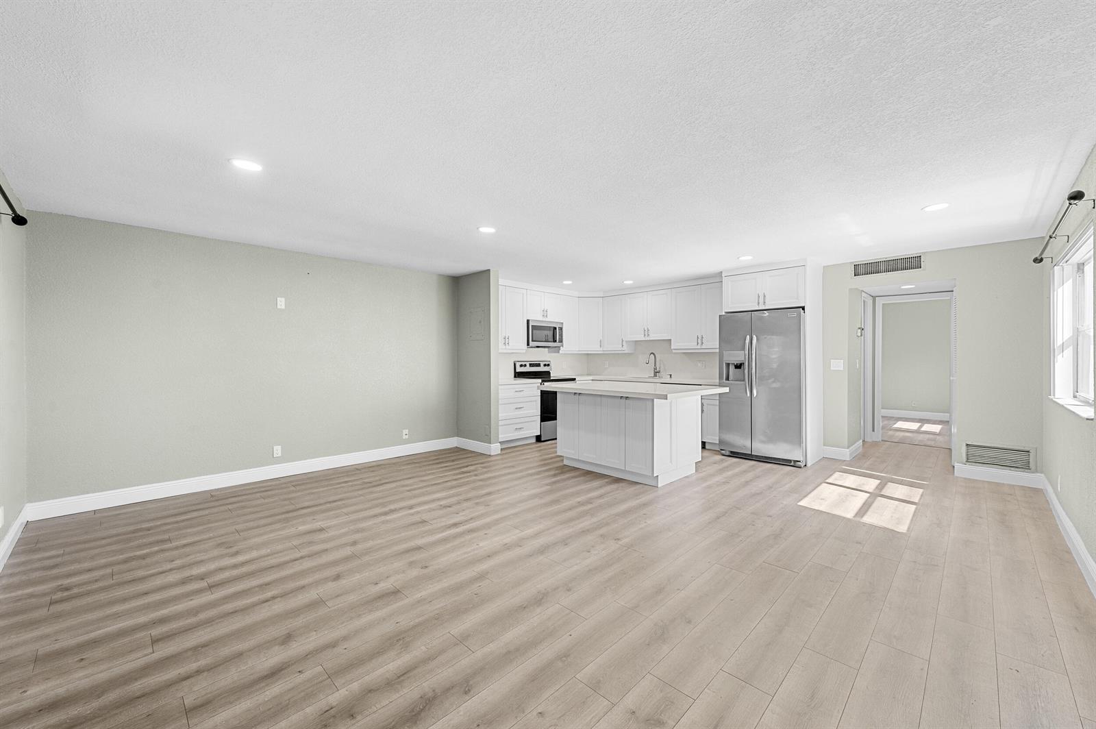 An open-concept kitchen and living area features white cabinetry, a central island, and wood-look flooring — 106 Tuscany B, Delray Beach FL 33446, DELRAY BEACH, FL
