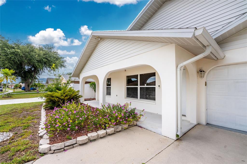 A white house exterior features arched porch openings, a concrete driveway, and a landscaped garden — 1458 STRADA D ARGENTO, VENICE, FL